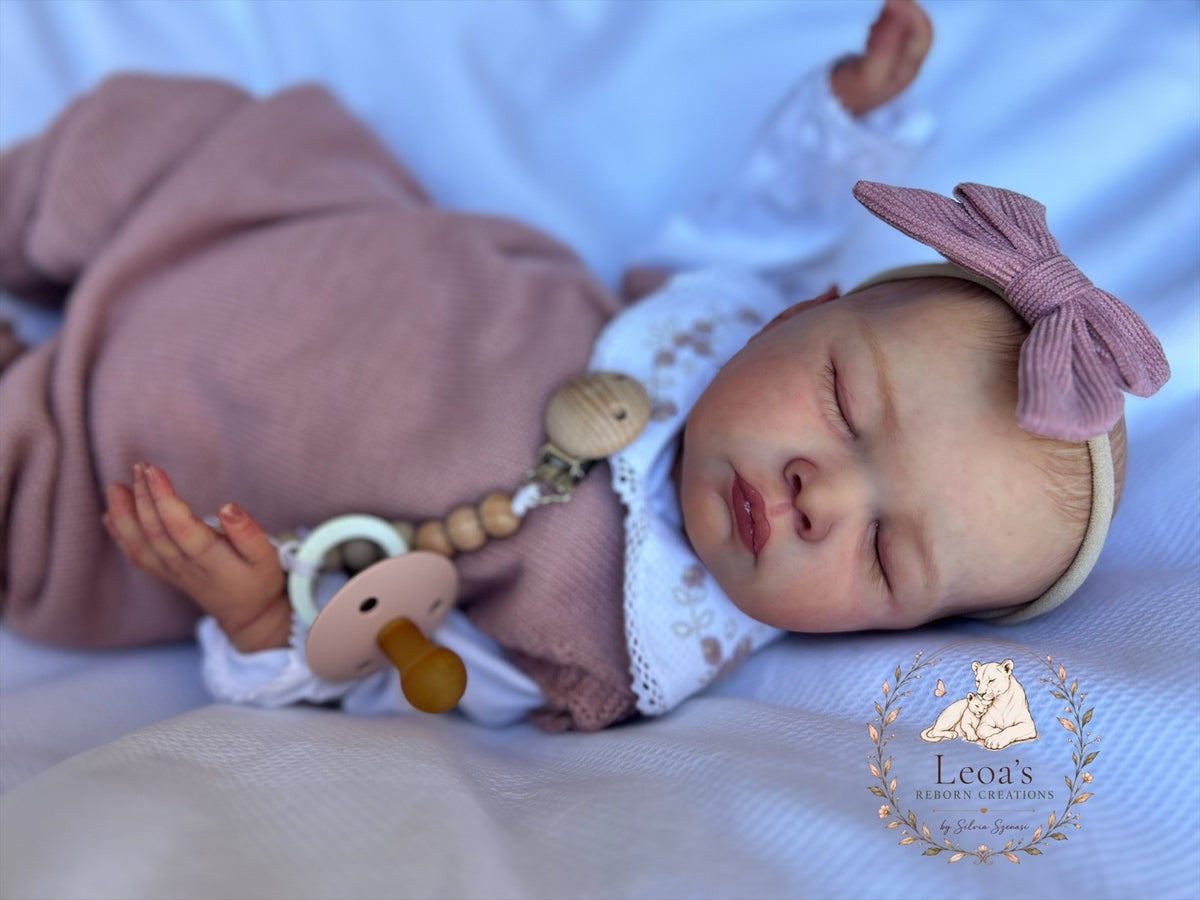 A reborn baby in white asleep beside a wooden 'Hello World' plaque