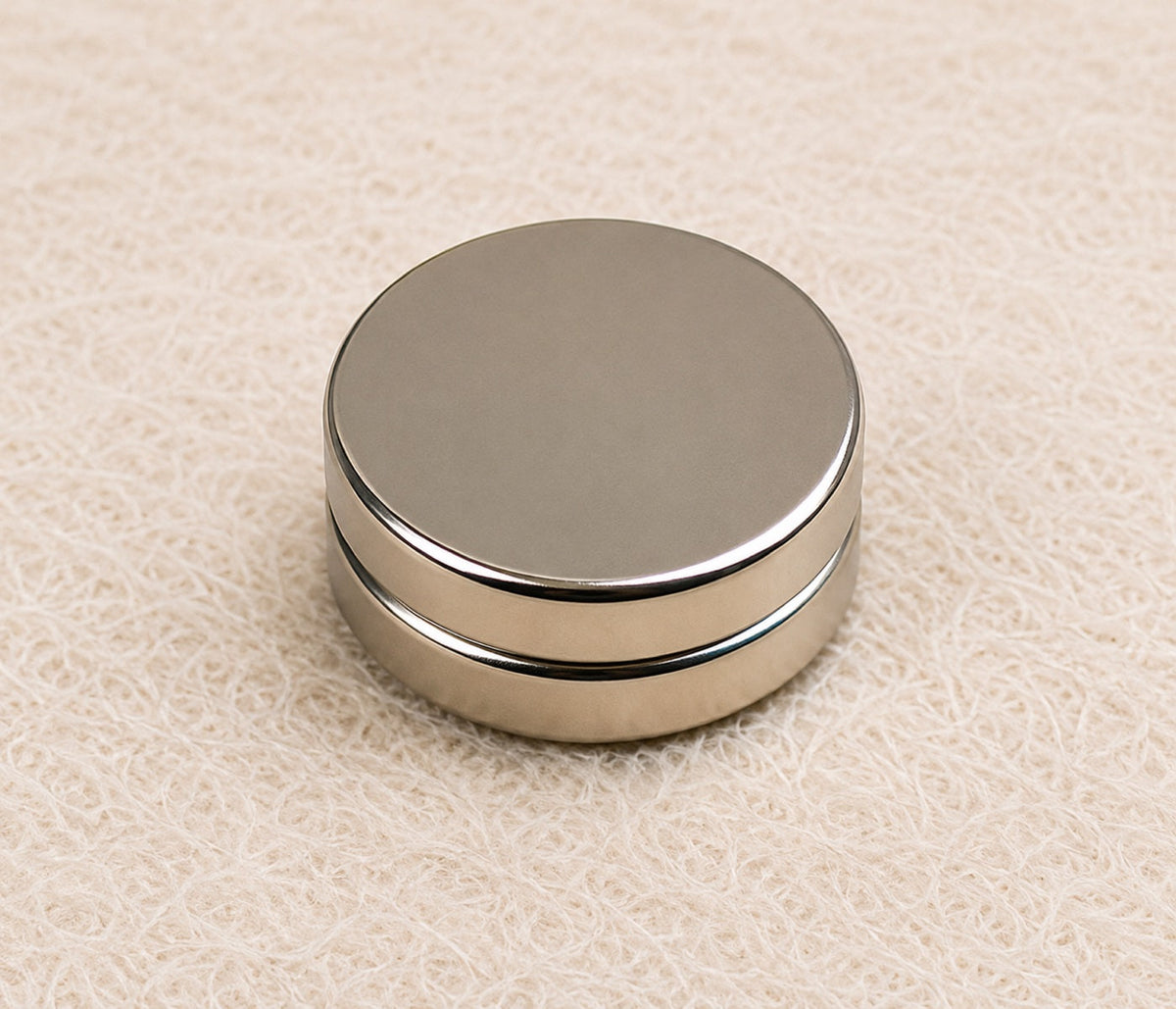 A 12mm by 3mm round neodymium magnet resting on a linen background